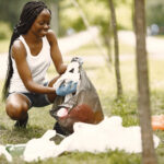 Volunteering and activism. Eco aware african girl is cleaning the park. She is putting trash into bag.
